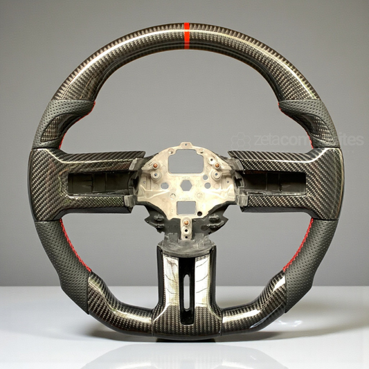 Carbon fiber steering wheel with red accent stitching, textured leather grip, center hub.