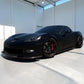 A matte black Corvette sports car with black wheels and red brake calipers, parked inside a bright, modern white garage.