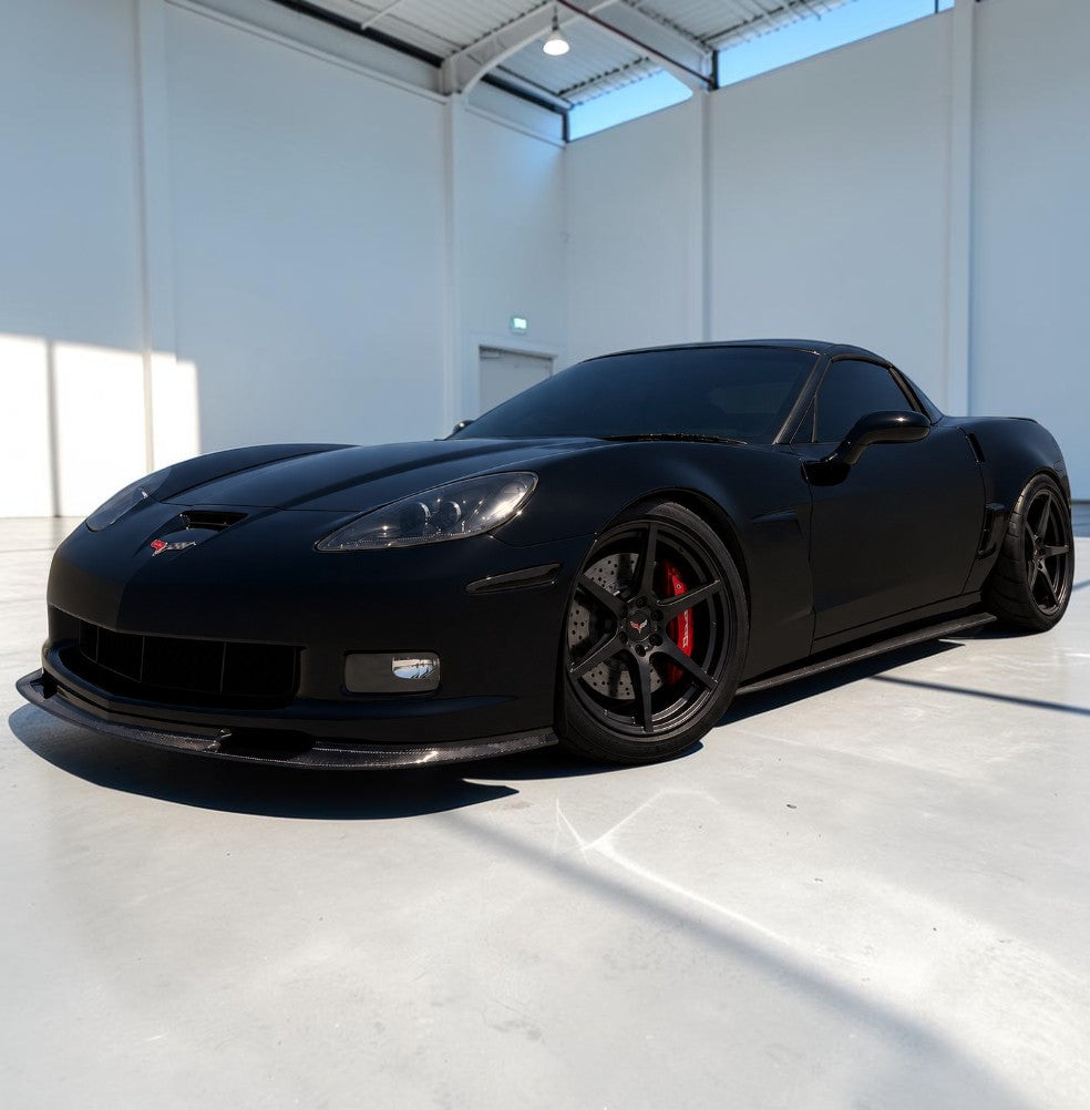 A matte black Corvette sports car with black wheels and red brake calipers, parked inside a bright, modern white garage.