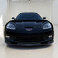 A black Corvette sports car photographed head-on in a clean indoor studio or showroom with white walls and floor.