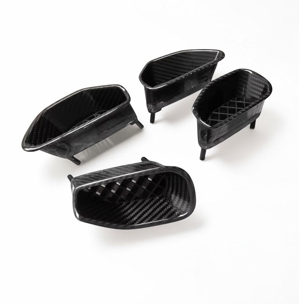 Four black carbon fiber textured automotive air intake or vent components arranged on a plain white background.