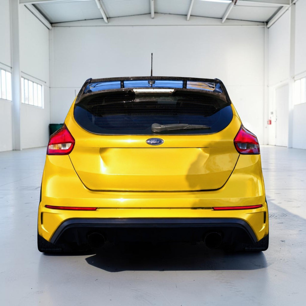 A bright yellow Ford Focus RS hatchback shown from the rear, parked inside a clean, white industrial showroom.