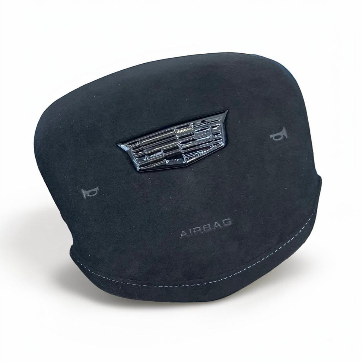 A black suede airbag cover with a metallic chrome Cadillac crest emblem and 'AIRBAG' text, shown on a white background.