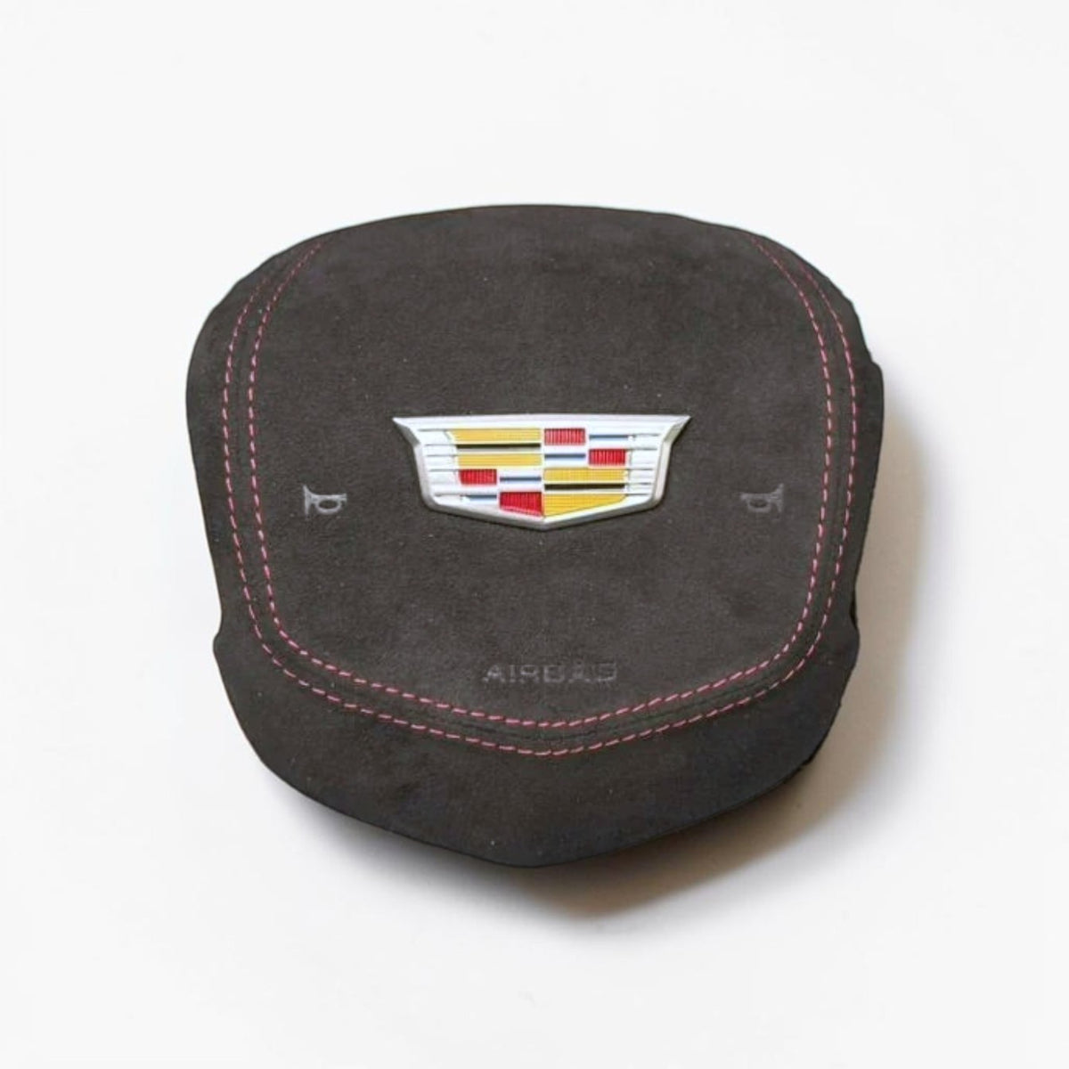 A dark gray suede or microfiber car airbag  cover featuring a metallic Cadillac crest emblem in the center, red contrast stitching, and the word 'AIRBAG' printed below.