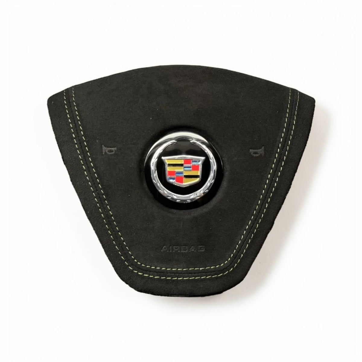 A black suede or Alcantara steering wheel cover with light contrast stitching and a central chrome-embellished Cadillac crest badge, shown on a white background.