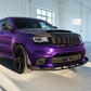A purple matte Jeep Grand Cherokee with a carbon fiber hood and custom black front grille and bumper lip, photographed in a bright, modern indoor studio with large windows.