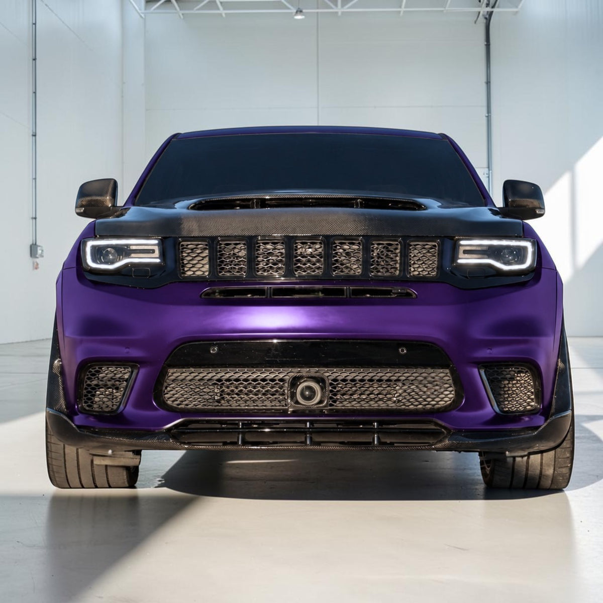 A front-facing view of a customized purple Jeep Wrangler with a black custom front bumper and grille, parked in a bright white studio.