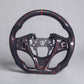 A carbon fiber sports steering wheel rim with red and black woven pattern, shown on a neutral gray background.