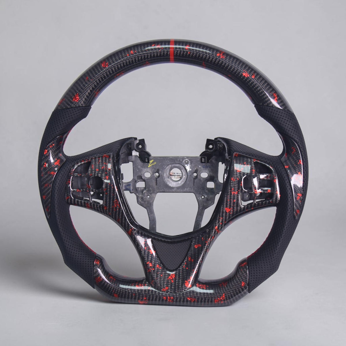 A carbon fiber sports steering wheel rim with red and black woven pattern, shown on a neutral gray background.