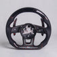 A carbon fiber sports steering wheel with a glossy black finish, red stitching, and red carbon fiber weave patterns, shown empty with the center console removed against a light gray background.