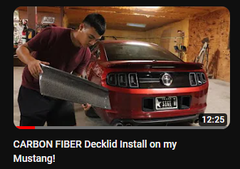 photo of a youtube thumbnail showing a man holding a carbon fiber decklid in preparation of installation on a 2010-2014 mustang